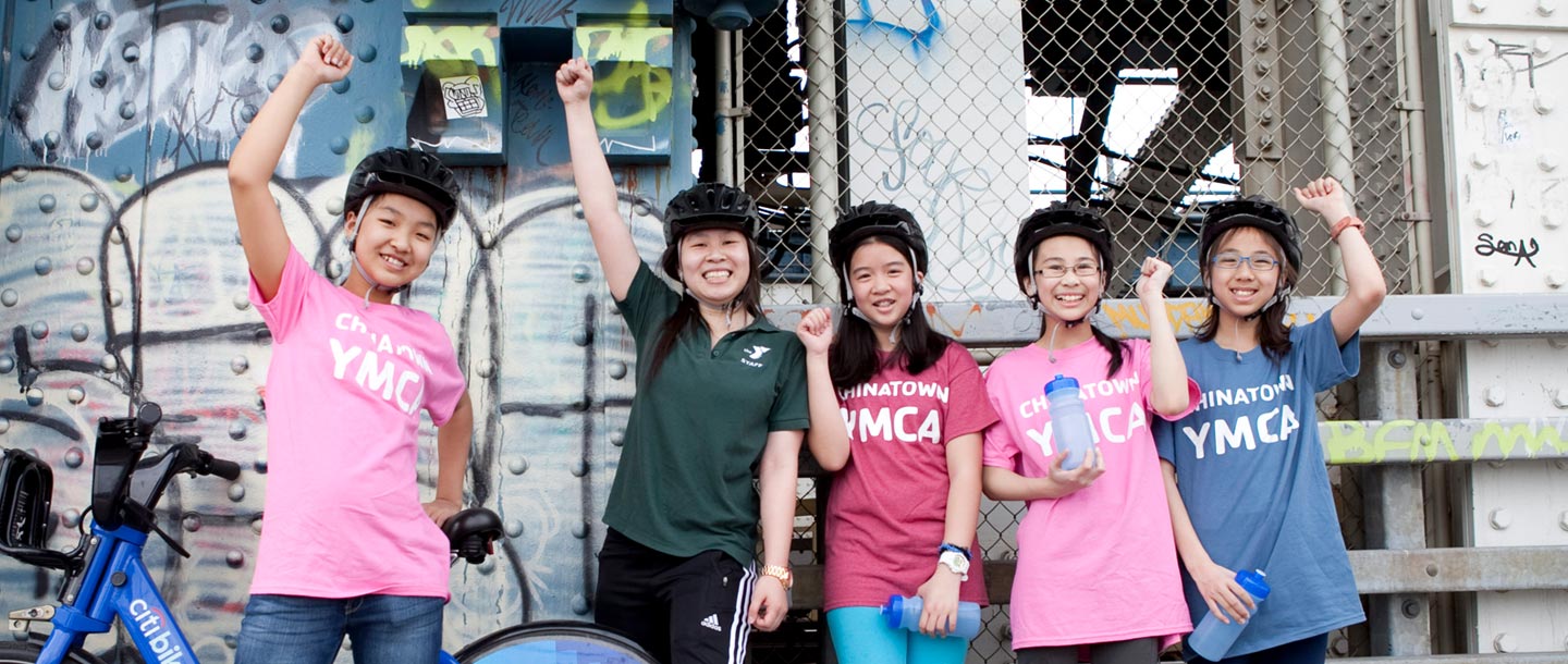 Five girls in YMCA tee shirts raise their fists and smile.