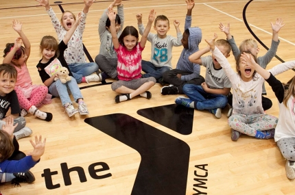 Kids sitting on the gymnasium floor around a YMCA logo.