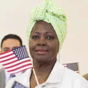 A woman wearing a head covering waves an American flag, surrounded by other people.