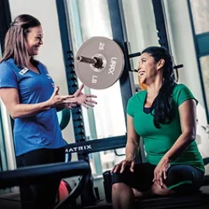 YMCA personal trainer smiling and laughing with fitness client in front of weight lifting rack machine at gym