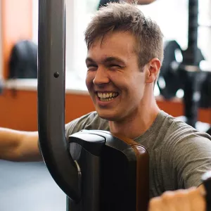 Man grins while using strength training machine for arms at Ridgewood YMCA fitness center