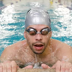 Man with goggles and swim cap takes breath at edge of North Brooklyn YMCA indoor lap swimming pool