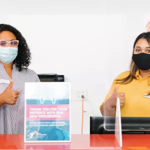 Two YMCA staff members wearing masks welcome members at the front desk of the Y.