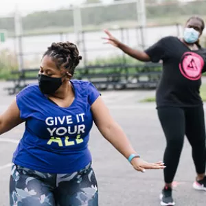 Two participants in masks in a YMCA outdoor Zumba class.