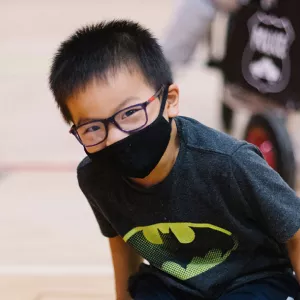 A boy wearing a mask smiles at the camera.