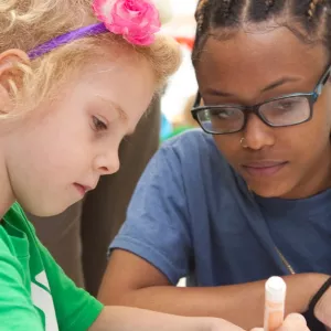 A counselor sits with a child as she colors at the McBurney YMCA summer day camp