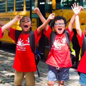 Four summer campers in front of school bus on field trip with Cross Island YMCA summer camp