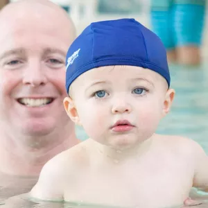 Dad with baby in blue swim cap swimming at YMCA indoor pool