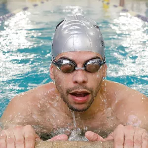 Adult wearing googles takes a breath on the side of North Brooklyn YMCA's indoor lap swimming pool