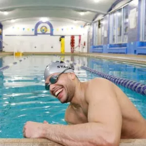 Man with cap and goggles smiling as he starts to swim at North Brooklyn YMCA's indoor pool