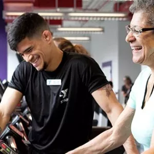 Personal trainer smiling while client walks on treadmill during training session